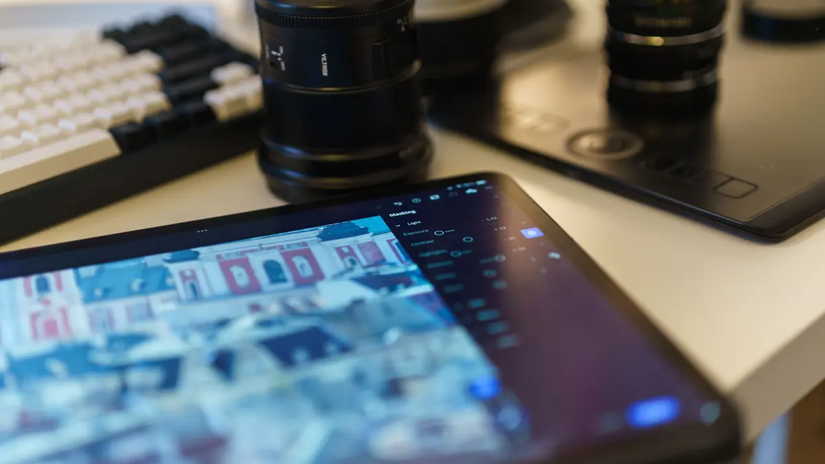 A modern workspace featuring a tablet, camera lenses, and graphic drawing tablet on a desk.