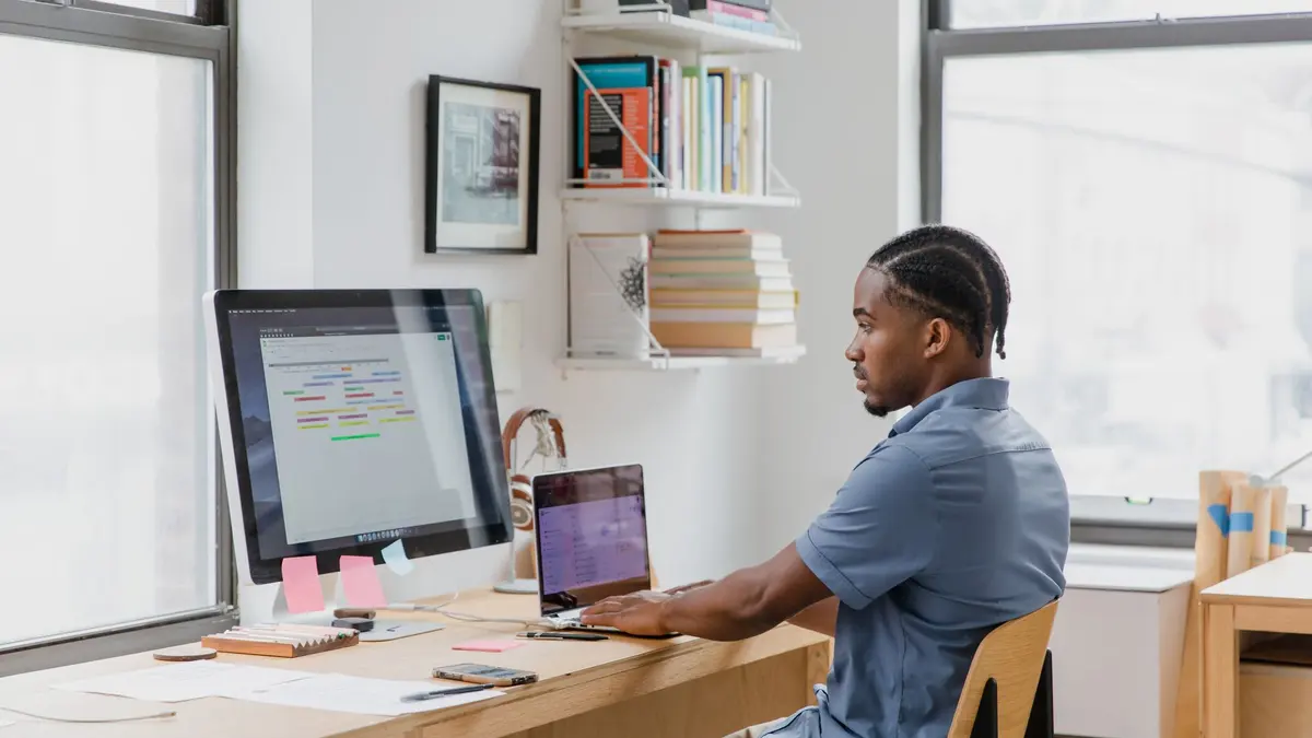 Focused man at home office desk working on dual screens. Ideal for remote work themes.